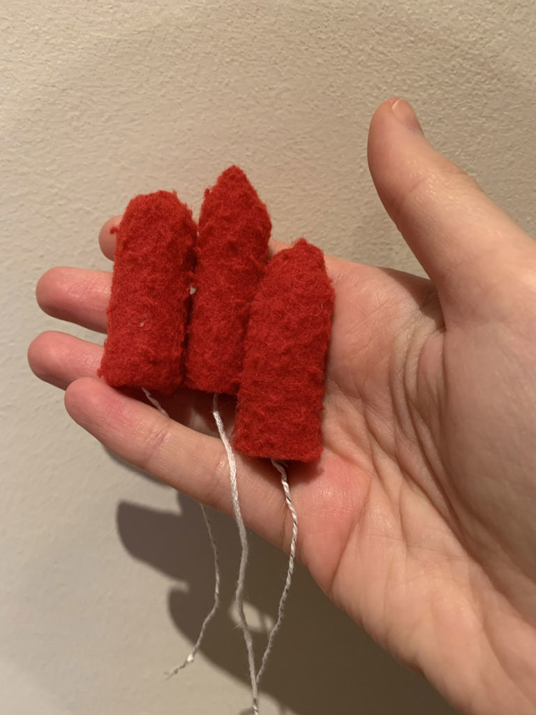 Hand holding 3 handmade and embroidered tampons, made from a St Andrews red gown